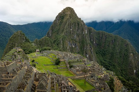 Majestic aerial shot of the iconic Machu Picchu surrounded by lush mountains under a cloudy sky,