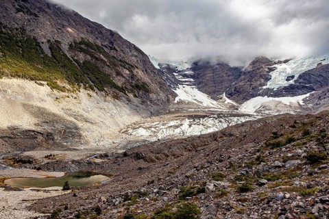 Rugged valleys with glaciers and scree, surrounded by high mountains under a cloudy sky - the