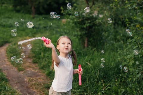 A joyful young girl delights in a summer day, playing with soap bubbles in a lush green outdoor
