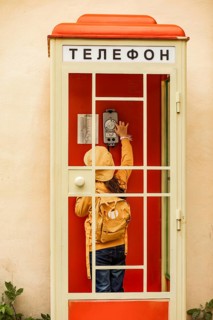 Unrecognizable preteen girl is seen reaching up to a vintage telephone inside a vibrant red booth.