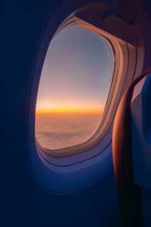 A serene sunset visible through the oval window of an airplane, showcasing a vast cloudscape tinged