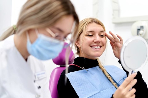 A patient is smiling and looking into a hand mirror after a successful check-up at a dental clinic.