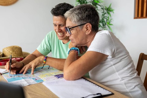 Two mature lesbian women joyfully plan their upcoming summer holidays, examining maps and browsing
