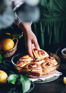 A hand reaches for freshly baked lemon rolls, perfectly golden and drizzled with glaze, in a glass