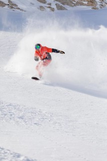 A snowboarder in vibrant gear expertly carves through fresh powder on a sunny mountain slope,