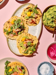 Top view of vibrant tacos prepared with sliced avocado, mango, fresh herbs, and salmon on a
