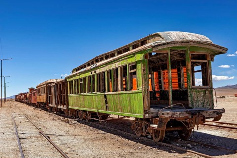 Abandoned green passenger car on rails in a desert landscape in sunshine, railroad cars in the town