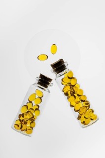 Two transparent glass bottles filled with yellow Omega-3 and Vitamin D capsules on a white