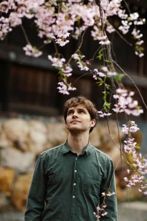 A man gazes thoughtfully at cherry blossoms in full bloom during sakura season in Japan, with the