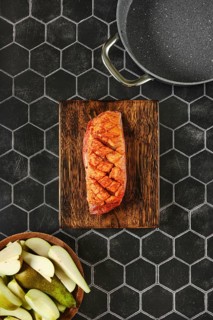 Top view of a juicy marinated spice rubbed duck breast on a wooden chopping board beside fresh