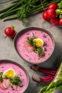 A bowl of vibrant cold beetroot soup, topped with slices of hard-boiled egg, fresh dill, and radish
