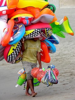 Flying merchant, seller overloaded with large quantities of beach toys, carrying many inflatable