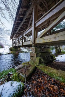 Wooden bridge over river in the forest, surrounded by snow and stones, Kälberbrücke, Enzklösterle,
