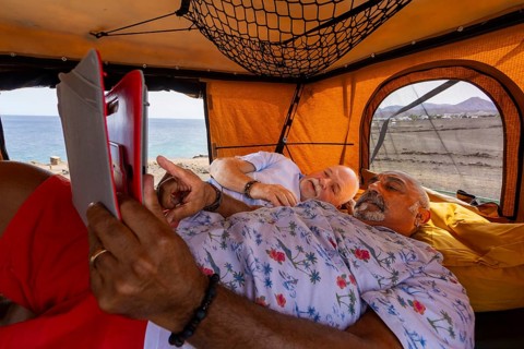 Gay senior couple enjoying a leisurely day inside their off-road camper, looking at a tablet with