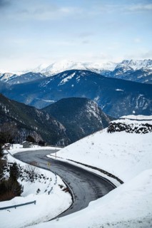 A scenic view of a winding road cutting through a snowy mountain landscape, bordered by pine