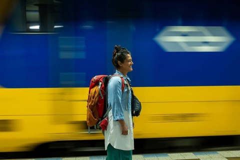 A traveler with a backpack smiles as a train speeds by at a station The scene captures the essence