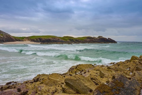 A wild coastline with breaking waves rolling across the rocks under a gloomy sky, Clachtoll Beach,