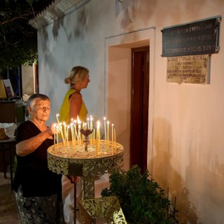 Elderly woman lights candles during a ritual near a church, festival, Panagia Kamariani, Megalo