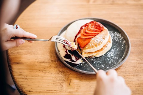 A plate of fluffy japanese pancakes topped with fresh strawberries, sweet syrup, and powdered
