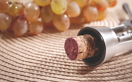 A corkscrew with a wine bottle stopper, lying on a woven napkin, with green grapes