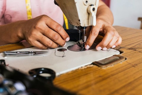 Hands of a asian seamstress using a vintage sewing machine to stitch fabric. The wooden table holds