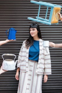 A stylish woman in a striped outfit poses in an urban setting, surrounded by a floating chair and