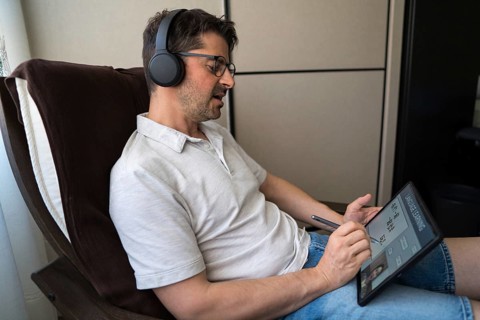 A man sits comfortably at home, focused on his tablet as he studies Mandarin online. Wearing