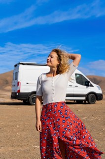 A woman enjoys a sunny day in Fuerteventura, Spain, with a camper van in the background. The scene