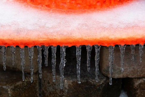 Close-up of icicles hanging from edge of flat base footing on orange fluorescent rubber traffic and