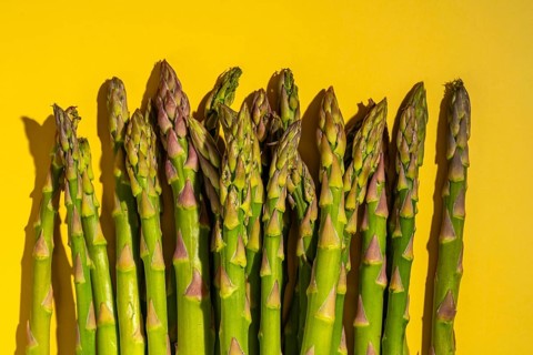 A bunch of fresh green asparagus spears is arranged against a vibrant yellow background, showcasing