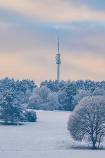 A tower rises above a snowy landscape with trees under a cloudy sky, district of Calw, Germany