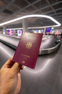 12.03.2026 hand holding German passport with baggage carousel in background at airport terminal,