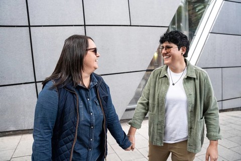 A joyous moment captured of a curvy lesbian couple, smiling and holding hands on a city street.