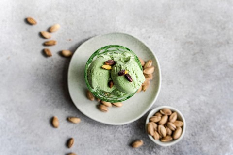 Two scoops of creamy pistachio ice cream sit in a glass bowl, garnished with whole pistachios. The