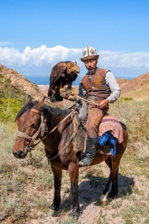 Traditional Kyrgyz eagle hunter with eagle in the mountains, hunting on horseback, near Kysyl-Suu,
