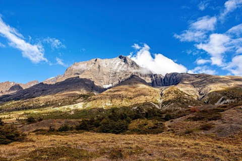 High mountain with hidden peak under blue sky and clouds, surrounded by green meadows, The