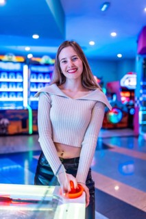 Smiling young woman enjoying a game of air hockey in a vibrant, colorful entertainment center