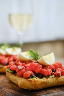 Freshly prepared open-faced sandwiches feature vibrant salmon chunks on mashed avocado and onion.