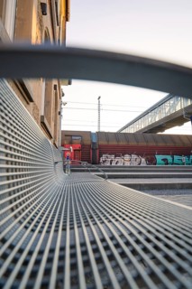 A metal bench at the railway station, accompanied by modern architecture and colourful graffiti