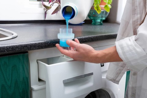 A Gen-Z girl pours vibrant blue liquid detergent into a cap in preparation for a laundry cycle,