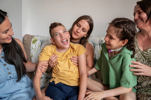 A joyful family shares a tender moment with a girl needing a tracheostomy and a boy with cerebral