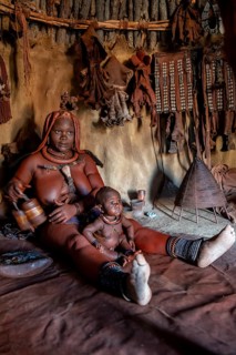 Himba woman sitting with baby in traditional hut, Himba village, Kaokoveld, Kunene, Namibia