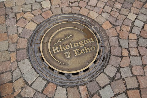 Round manhole cover with the inscription Mitten drin Rheingau Echo, paving stones, soil, Eltville,