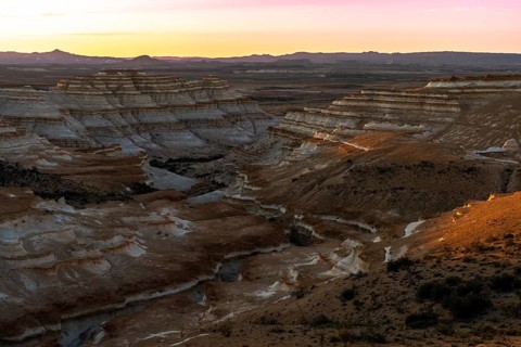 Eroded sedimentary rock formations with layered rock walls and gorges in a semi-desert landscape at