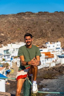 Young man sitting on a wooden pole enjoying the view of the colorful houses of tufia, a coastal