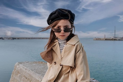 A young girl in trendy attire stands by the waterfront in Civitanova, Italy. Her stylish trench