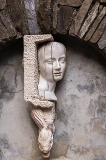 Close-up of white sculpted head and serpent on water fountain and arch made of old stones,