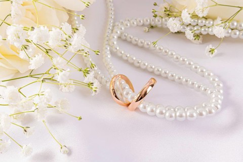 Elegant wedding rings paired with delicate flowers and a string of pearls on a soft white