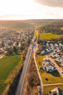 Aerial view of a village with railway line and surrounding natural landscape in evening light,