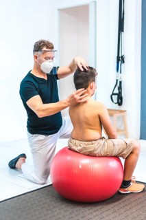 Physiotherapist with mask and screen looking at a child's neck. Reopening with security measures of
